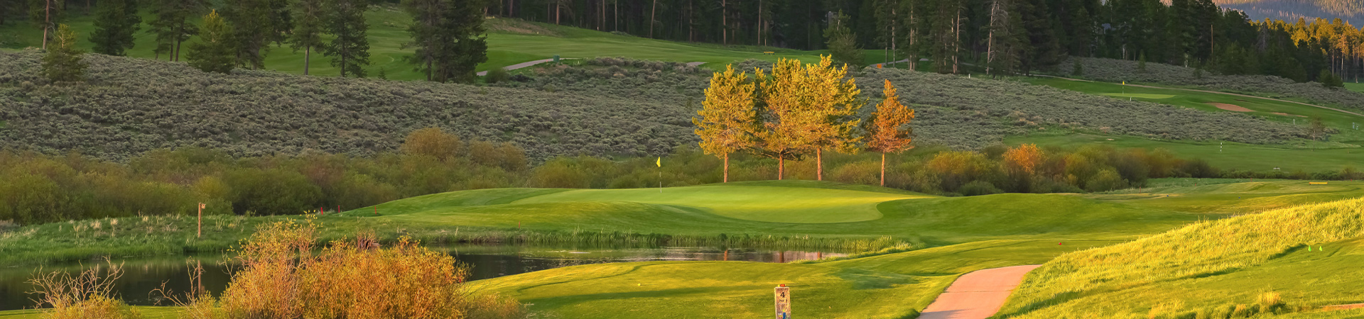 Panoramic view of a serene golf course at dusk, showcasing lush greens in the foreground with a flagstick and hole visible.