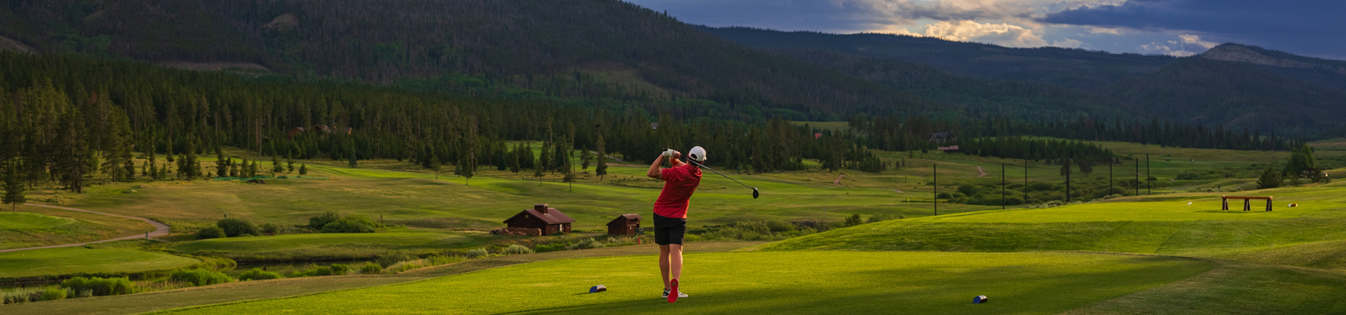 A golfer in a red shirt and white cap is captured in mid-swing on a lush golf course.