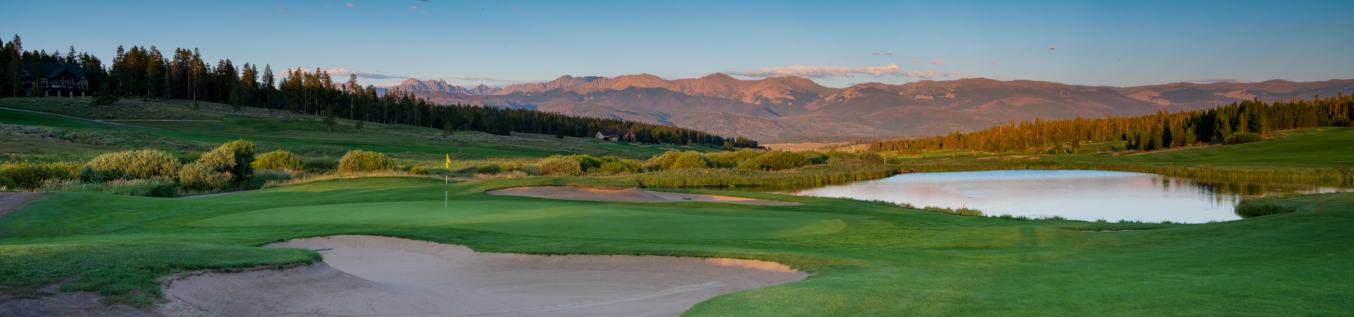 A panoramic view of Pole Creek Golf Club at dusk, featuring an expansive green with a prominent sand bunker in the foreground.