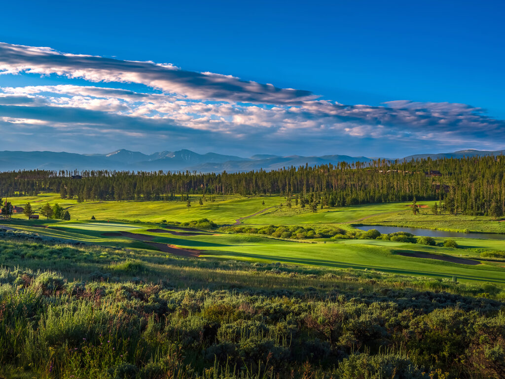 An early morning view of Pole Creek golf course with vibrant green fairways, punctuated by dark green patches of trees and interspersed with sand bunkers and a calm pond. 