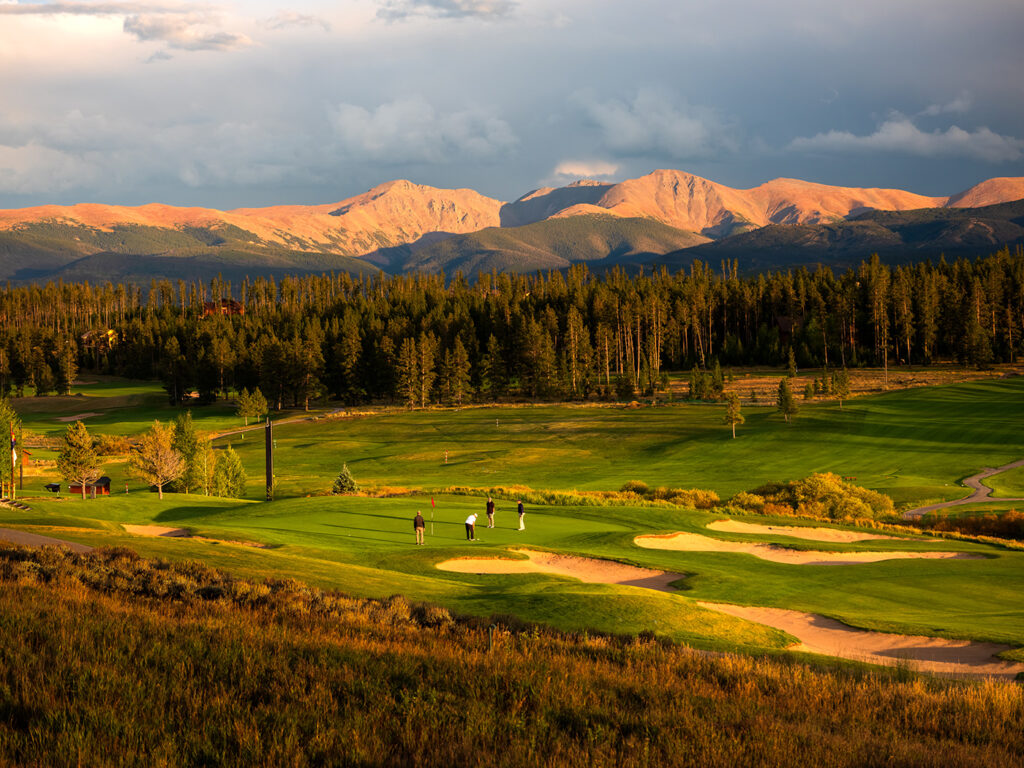 A group of golfers putting on a green at Pole Creek Golf Club during a captivating sunset. 
