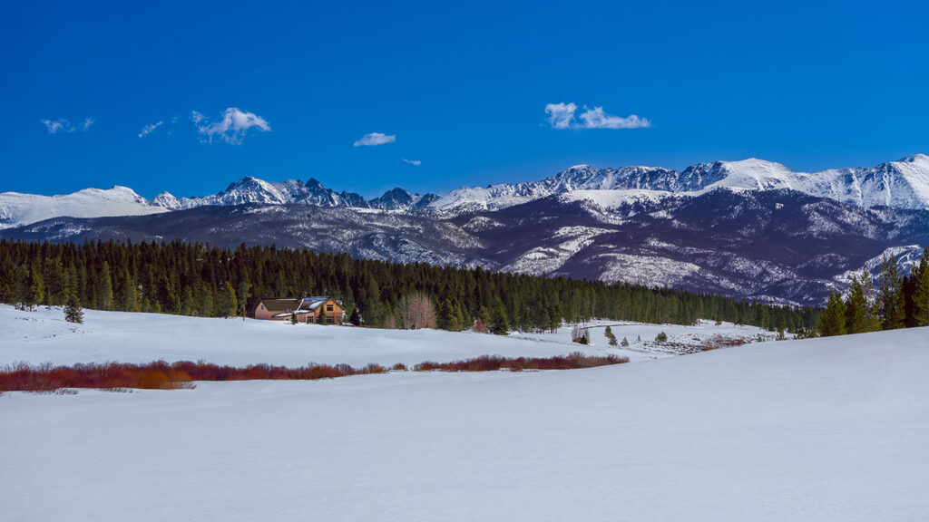 The expansive snow-covered landscape of Pole Creek Golf Club in the foreground, with a lone clubhouse visible amidst vast snowy fields and evergreen trees.